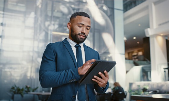 A professional in a suit stands in a modern lobby, using a tablet.