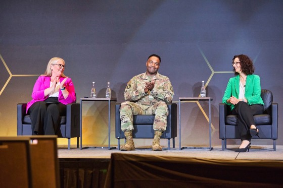 Two women and one man on stage in business and military dress for a panel discussion