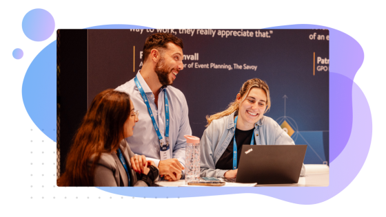 Three people chatting at a conference in front of an open laptop