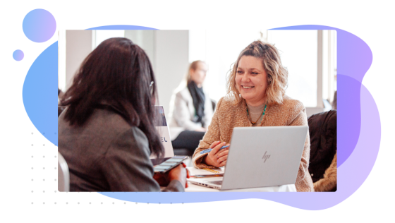 Two women chatting at a table with an open laptop in front of them
