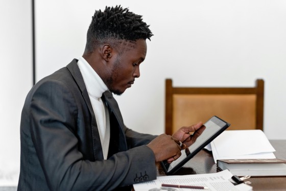 Man in white turtleneck and grey coat working on a tablet in an office