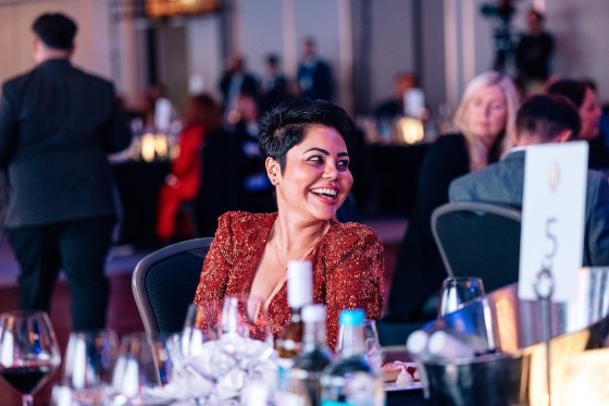Woman in red dress with short hair laughing at dinner table at awards gala 