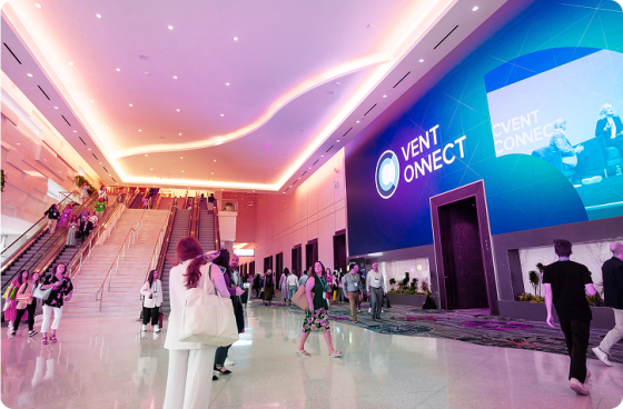 Attendees walk through a large, bright convention center lobby with escalators on the left and a massive digital screen on the right displaying the Cvent CONNECT logo and event imagery.