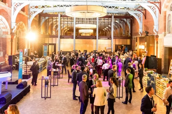 Professionals networking at a cocktail reception in a grand historic venue with ornate arched architecture.