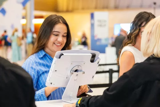 Smiling woman looking at a tablet kiosk display while others stand nearby.