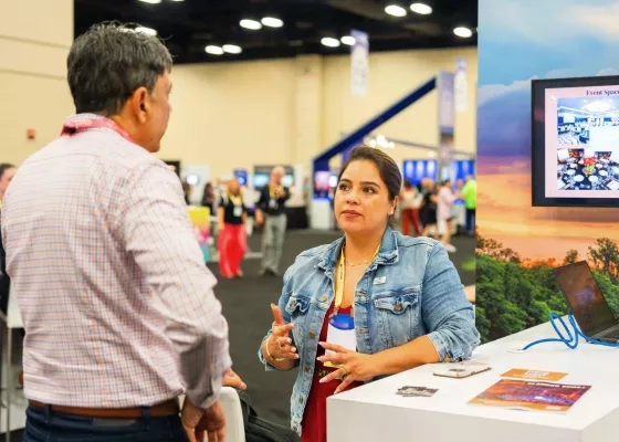 Woman in a denim jacket gesturing while explaining something to a man at an expo booth.