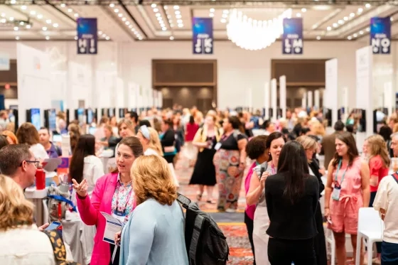Crowded conference expo hall with attendees mingling near booths and hanging signage.