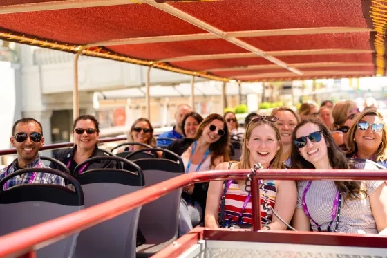 Group of smiling conference attendees riding an open-top tour bus.