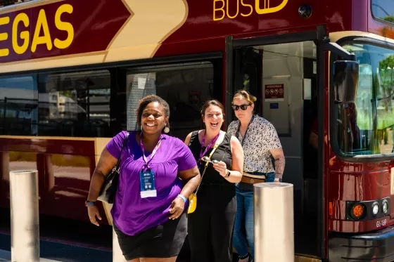 Three laughing women exiting a red double-decker "Vegas" tour bus.