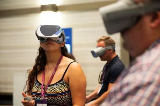 Conference attendees wearing virtual reality headsets and holding controllers during an event session.