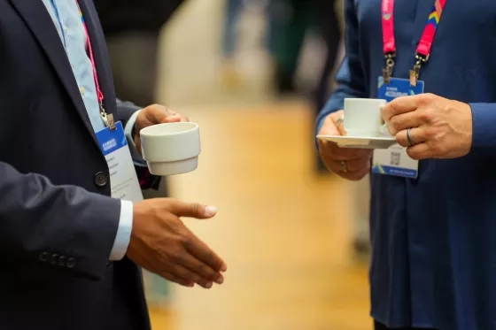 A closeup of two peoples' hands holding small espresso cups while wearing conference lanyards.