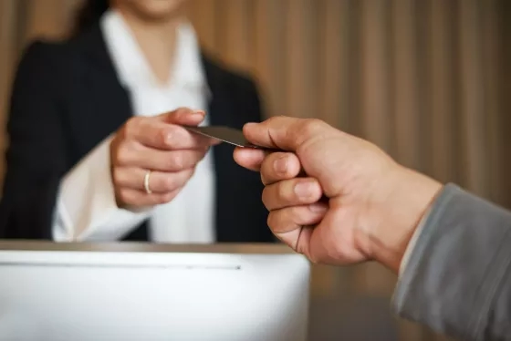Hand exchanging a credit card with another person at a reception desk.