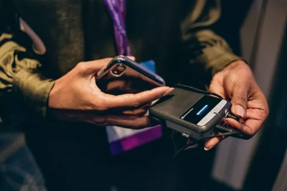 Hands adjusting a wireless microphone transmitter pack next to a smartphone.