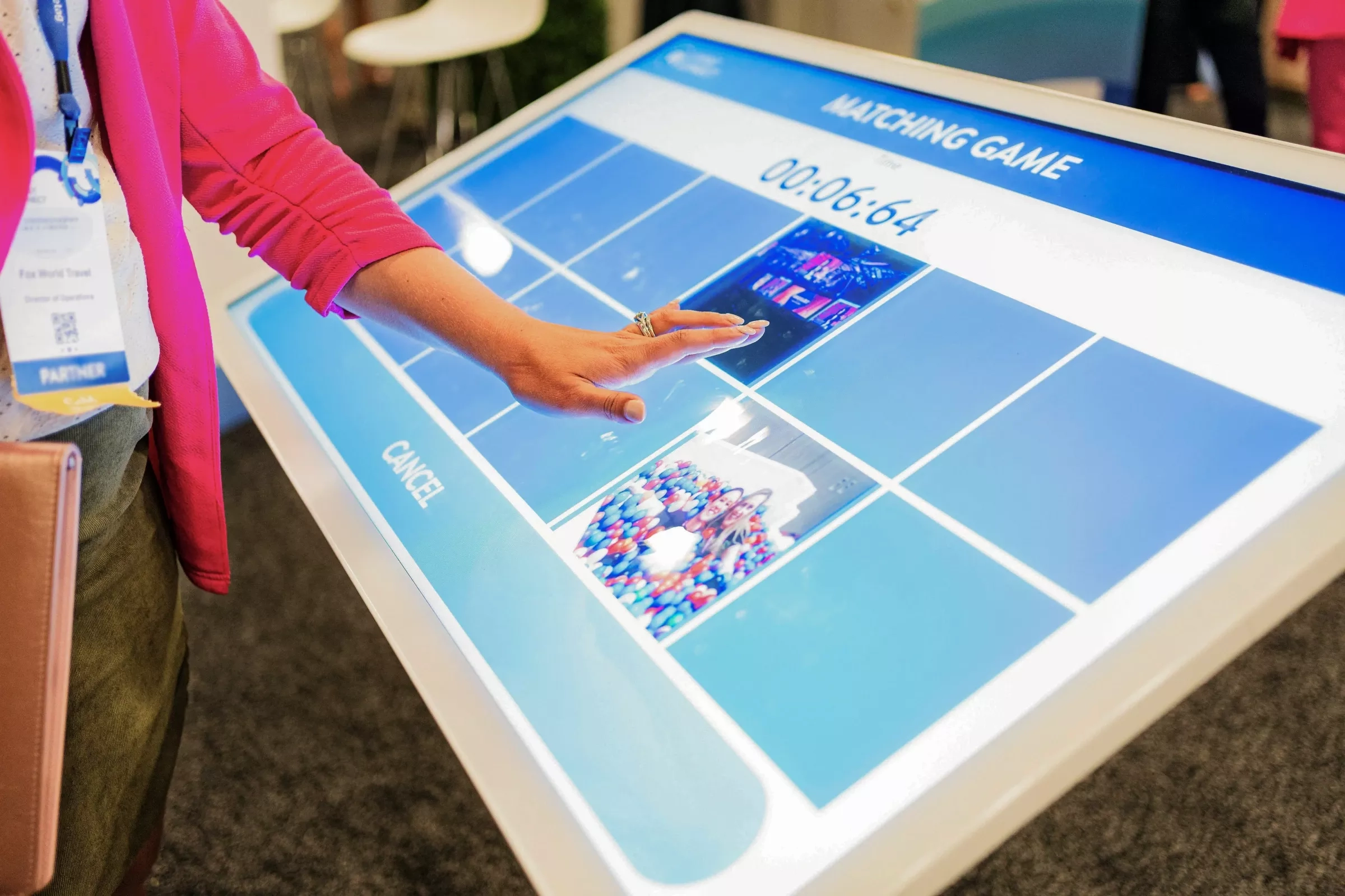 Hand touching a large interactive touchscreen table displaying a "Matching Game" with photo tiles.