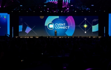 A person stands on a stage, giving a speech to a crowd at a Cvent Connect event.