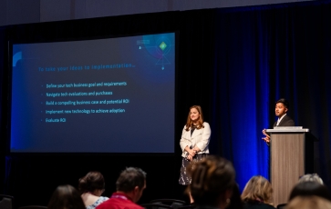 A man stands at a podium giving a presentation on a large screen in front of an audience.