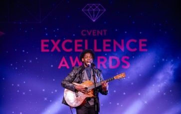 A man performing at the Cvent Excellence Awards with a guitar in front of a starry background.