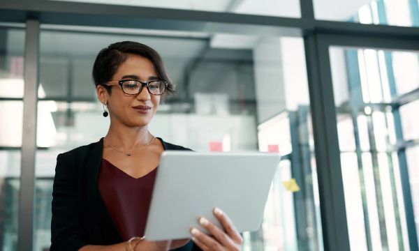 Female standing in an office holding a tablet and looking at the camera with a smile.