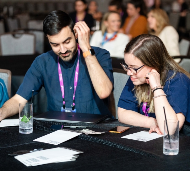 A man and woman are sitting at a table, working on their laptops at Cvent CONNECT 2023.